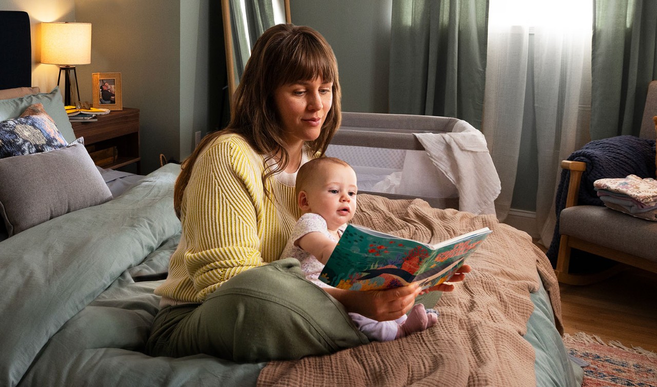 Woman sitting on bed reading to baby